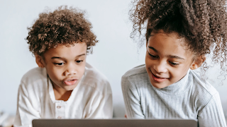 Two black siblings, a boy and a girl watching a laptop and chatting