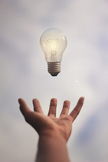 A hand reaching out to catch an airborn incandescent lightbulb