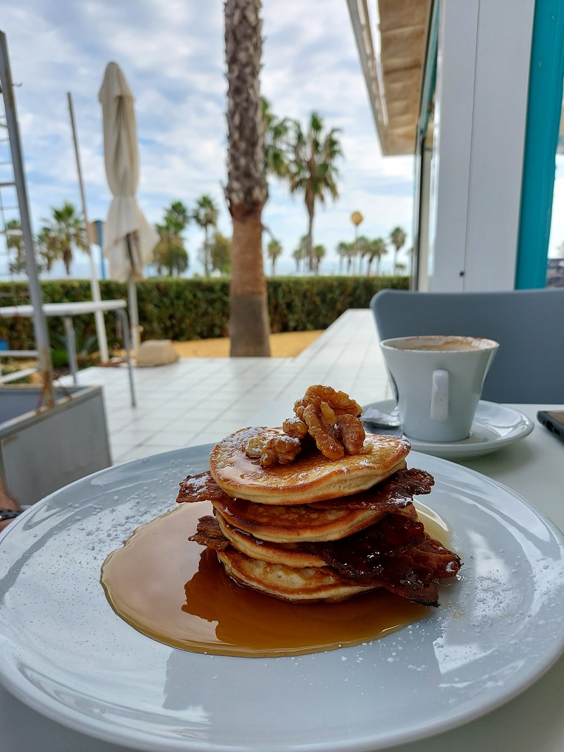 Pancakes with bacon and maple syrup, topped with walnuts, with Playa Flamenca in the background