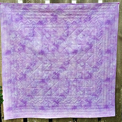 A lavender colored wholecloth quilt with a central star motif