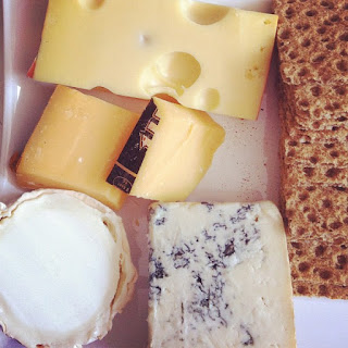 A platter containing four types of cheese, and crackers.