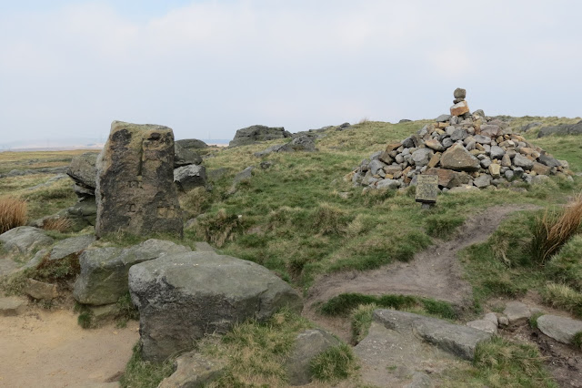 An old stone post on the left with carvings and a large stone cairn to the right.