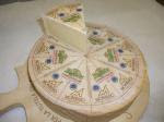 A photo of a wheel of Montasio cheese with a wedge of cheese cut out