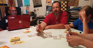 A game of Stipulations: people sitting around a table reading what players have written on their cards