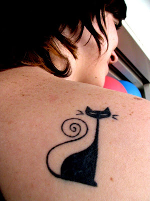 A cool and cute tattoo of animated black cat at the back of the shoulder.