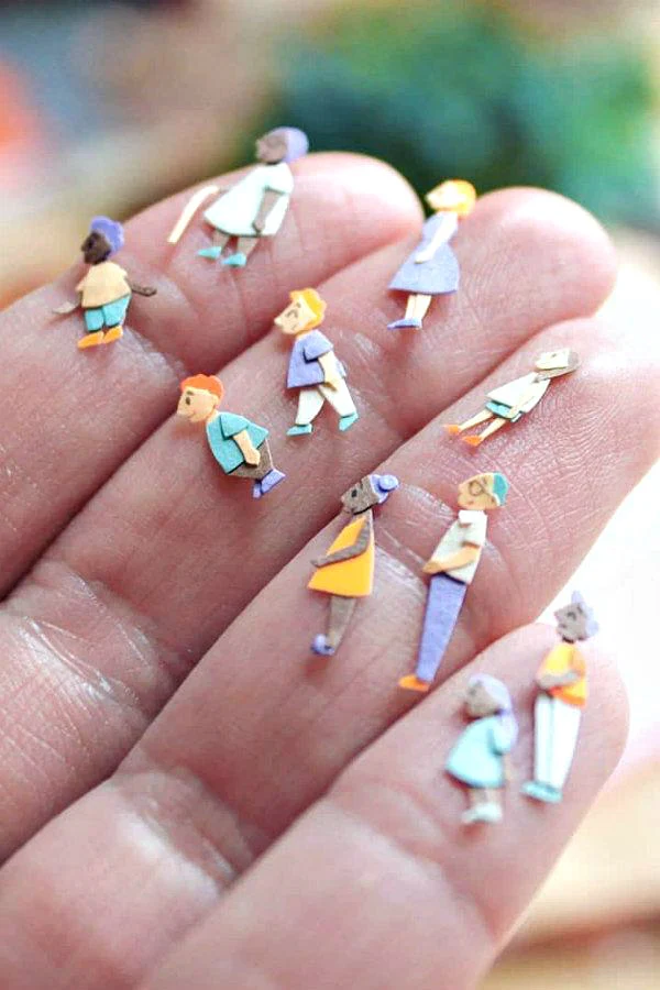 miniature, colorful paper cut figures shown on a hand for scale