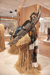 Photo of museum exhibit African Mask with Grass Skirting and Draped Cape.