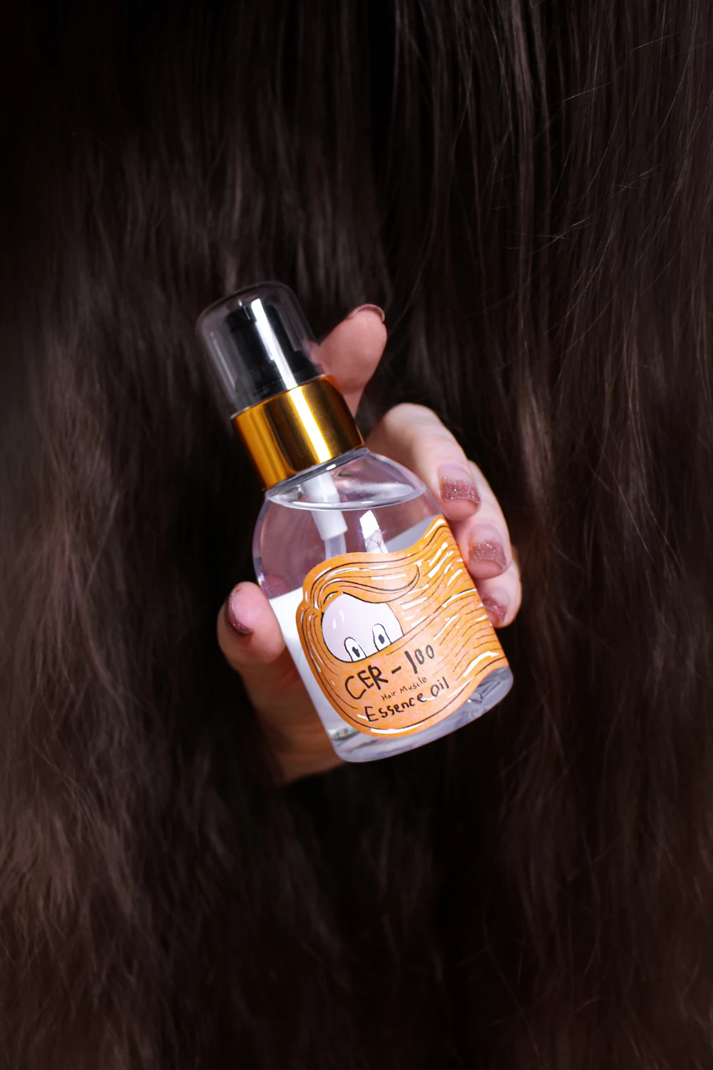 a female hand covered in long, luscious hair holding a tube of cer-100 essence oil by elizavecca