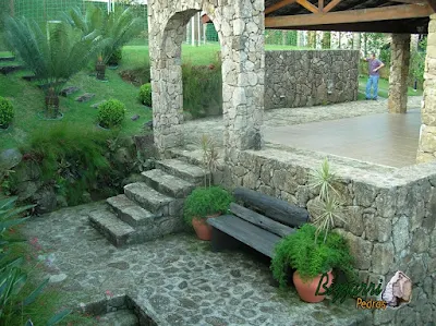 Construção do muro de pedra com pedras brutas com o piso de bruta com a escada de pedra, o pórtico de pedra com a escada de dormente de madeira e a execução do paisagismo em sítio em Mairiporã-SP.