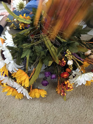 A pile of fake flowers, mainly yellow and white sunflowers, with a few red and purple roses and red-to-yellow millet heads, and a dramatic orangey-red motion blur above the pile.