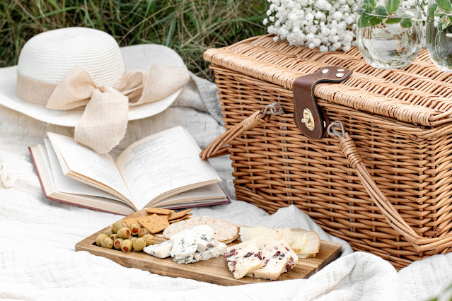 Picnic basket and grazing board on blanket with hat and book:Photo by Evangelina Silina on Unsplash
