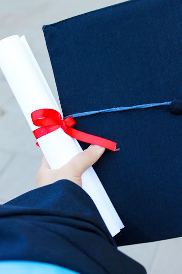 hand in graduation gown clasp rolled up diploma and graduation cap