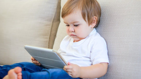 A small kid holding and watching a tablet