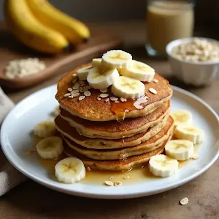 A stack of golden-brown banana and oatmeal pancakes topped with fresh banana slices, a drizzle of honey, and a sprinkle of oats, served on a white plate in a cozy kitchen setting.