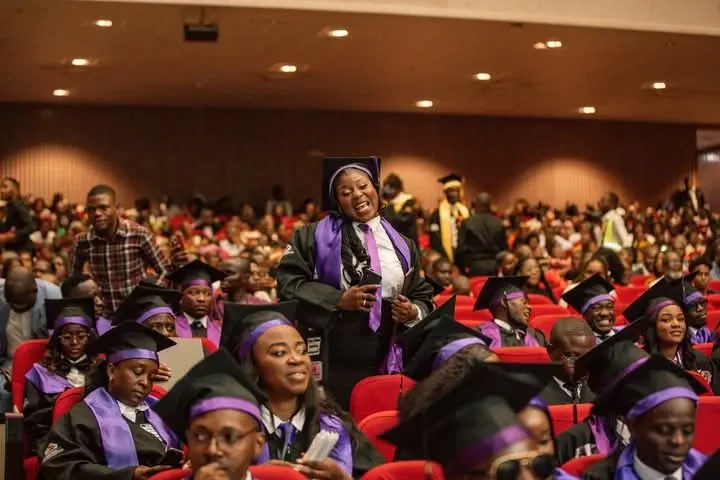 Celebração de formatura com estudantes felizes em um auditório. A multidão demonstra orgulho e animação durante a cerimônia.