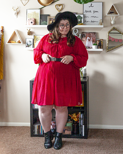 An outfit consisting of a black floppy hat, a red long bishop sleeve pleated midi dress, belted, and black Chelsea boots.