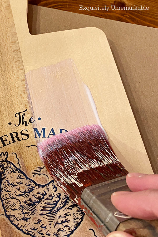 A paint brush applying sealer to wooden sign cutting board