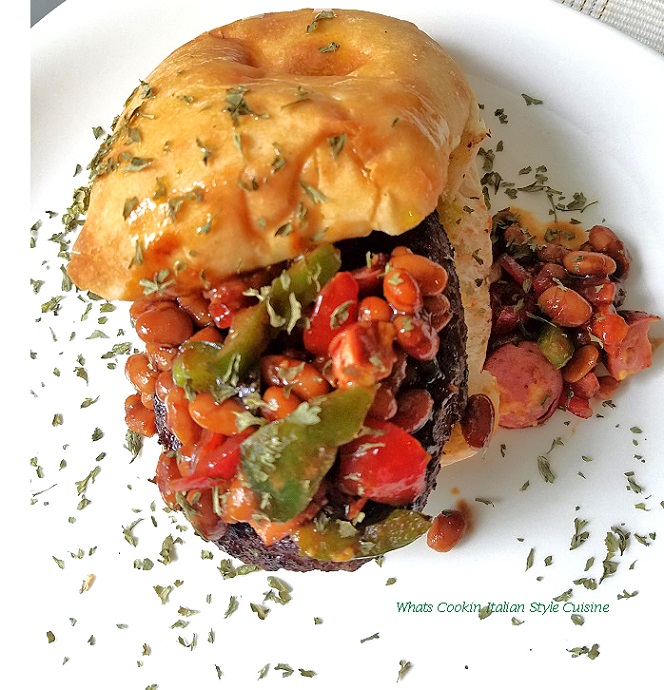 this is how to make a chili with hotdogs in it then added to a grilled hamburger on a ciabatta roll. This is sitting on a white plate with sprinkles of dried parsley and more chili falling off the burger.