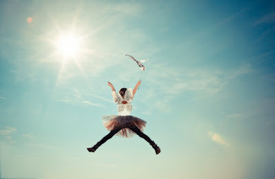 A girl, dressed as a fairy princess, jumping for joy, in bright sunlight.