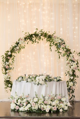 sweetheart table with white floral and round floral arch behind it