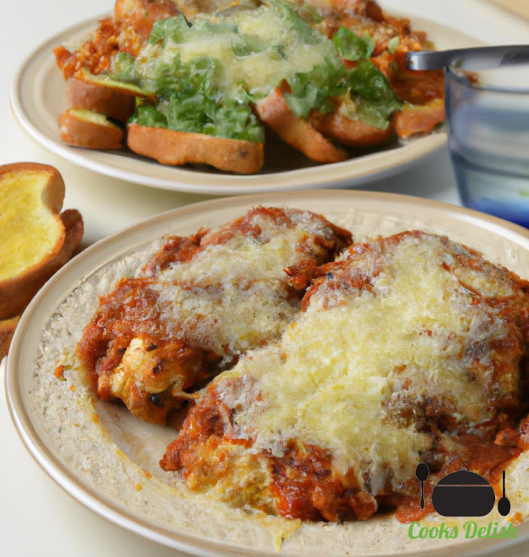 Close-up of a baked chicken parmesan on a plate. The breadcrumbs are golden brown and crispy, and the chicken is coated in a tangy marinara sauce and topped with melted mozzarella cheese. The garlic bread is crispy and buttery.