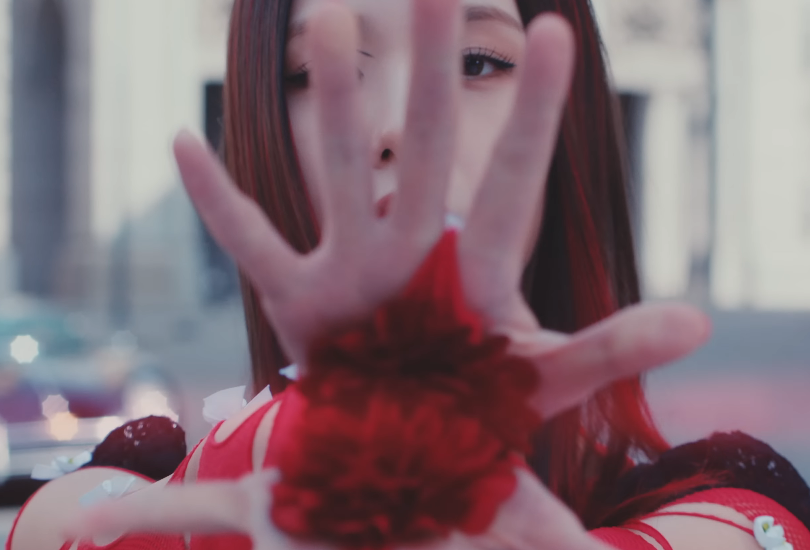 A screenshot of Jisoo in the music video for her solo debut song “Flower”. Holding her palms out to the camera, displaying flowers which are part of her outfit.