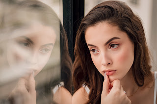 young woman thinking with mirror to her right.