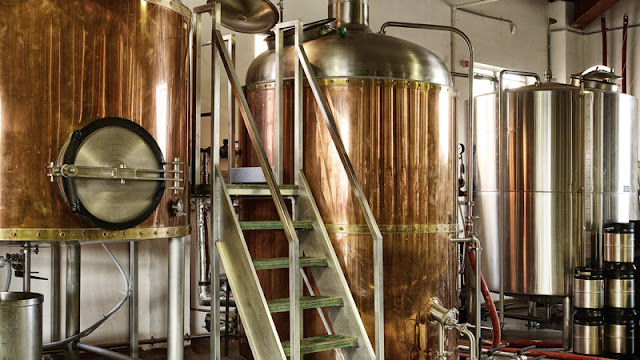 several copper brewing tanks so large that a ladder is needed