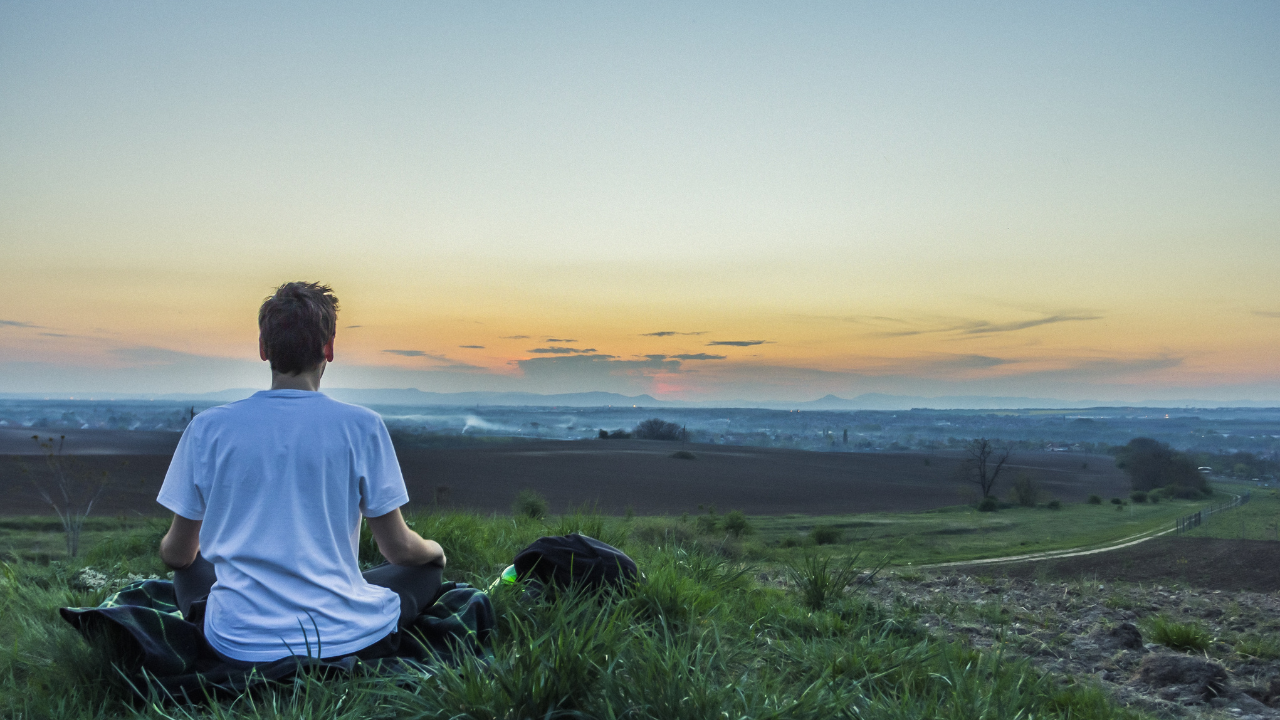 a person meditating in a field at sunset - meditation