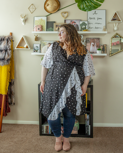 An outfit consisting of a white on black polka dot wrap dress with black on white ruffles and sleeves over blue jeans and pink pointed toe mules.