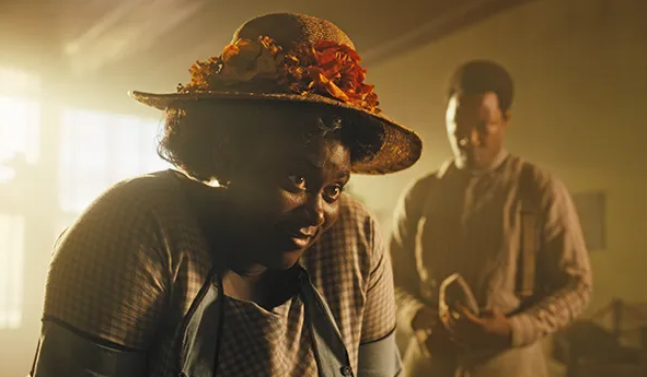 a Black woman with a beautiful hat leans in to a table