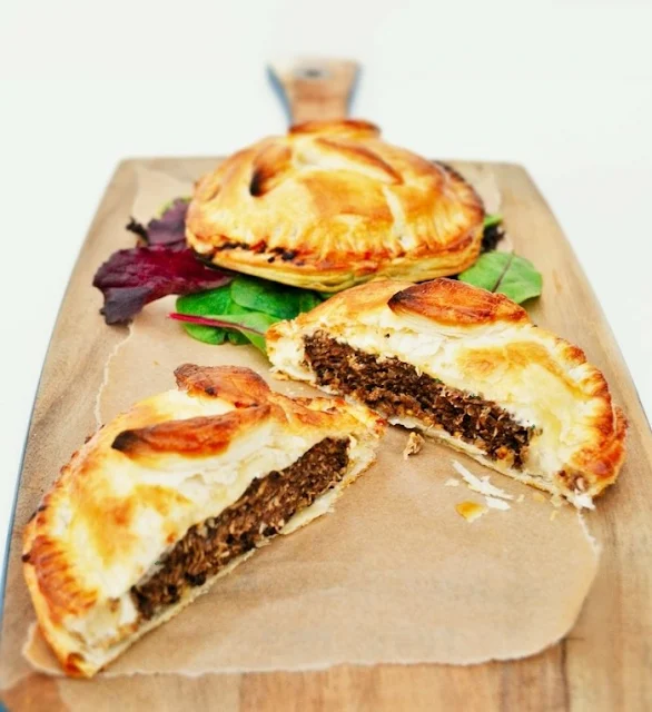Vegan burger pies on a wooden board, one cut open showing the layers.