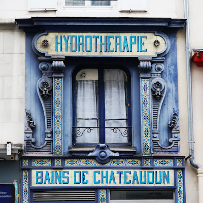 A building facade with ornate, blue-painted woodwork; tiling says 'Hydrotherapie' and 'Bains de Chateaudun'.