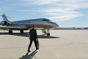 Source: VistaJet. A man in a business suit walks across the tarmac towards a VistaJet plane in red and silver livery.