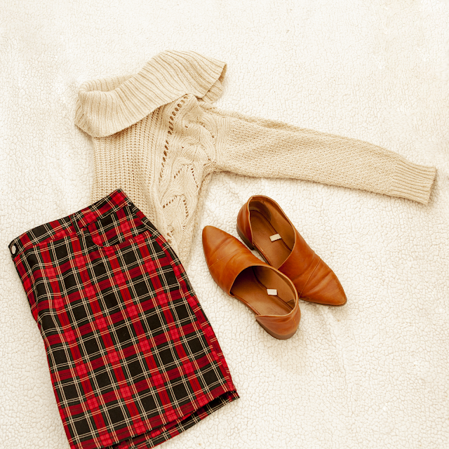 A flatlay of a cream cowl neck sweater, a red and black plaid mini skirt and brown d'orsay flats.