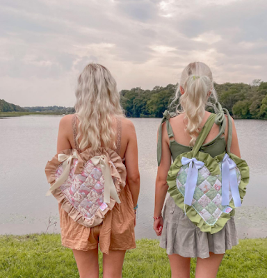 arries a charming pink bag, while Emmy adorns a stylish green one. The picturesque backdrop features a scenic landscape with a flowing river and lush green mountains, adding to the enchanting ambiance. These handmade bags reflect the creativity and craftsmanship of the talented duo