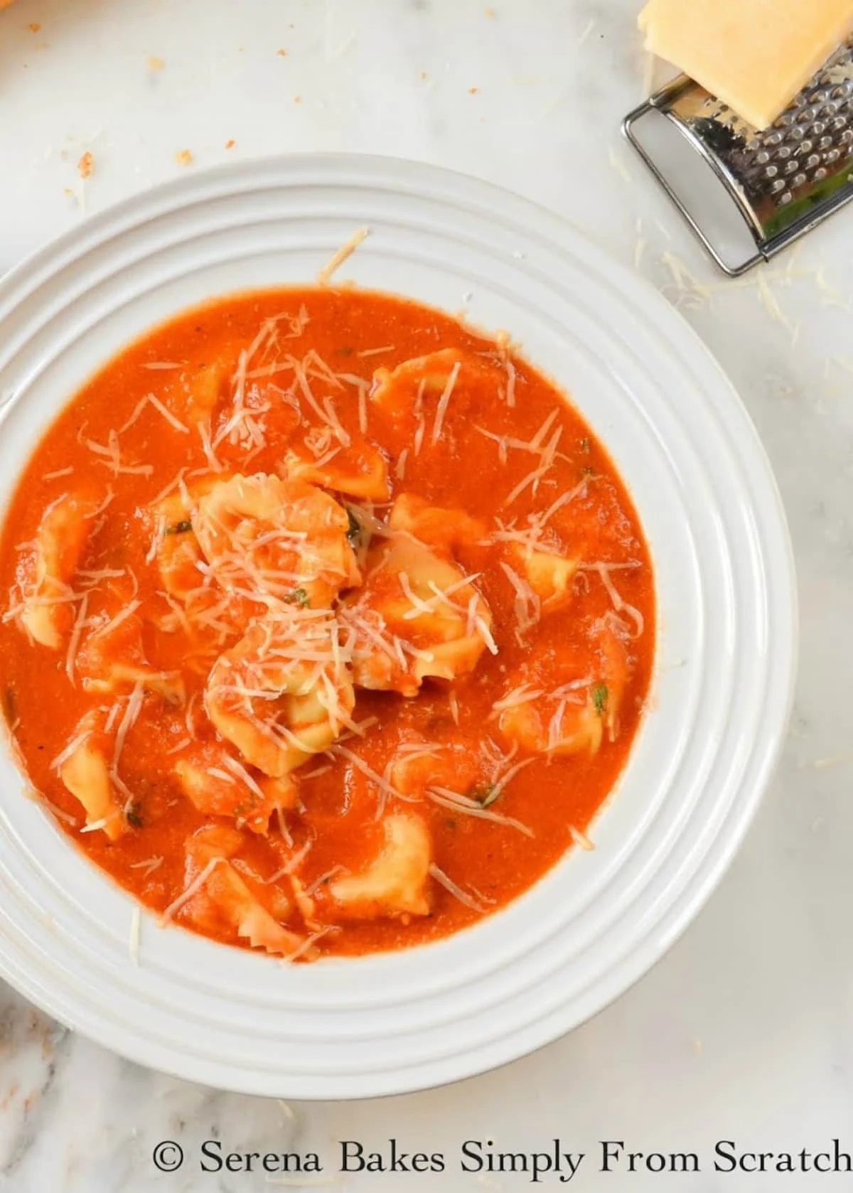 A down shot of Creamy Tomato Tortellini Soup in a white bowl topped with grated parmesan cheese.