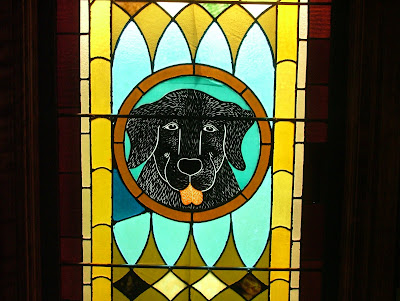 A stained glass window of a black dog looking forwards