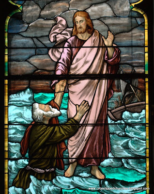 Close up of stained glass window of Jesus walking on water reaching out to Peter.