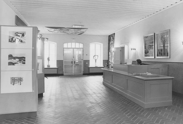 Lappeenrannan taidemuseo; mustavalkoinen sisäkuva lipunmyynnistä, avoinnapitäjä tiskin takana.