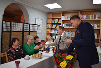 Burmistrz Zelowa pan Tomasz Jacymek oraz Radny Rady Miejskiej Mateusz Rogut wręczają kwiaty przybyłym na spotkanie z okazji Dnia Kobiet czytelniczkom biblioteki.