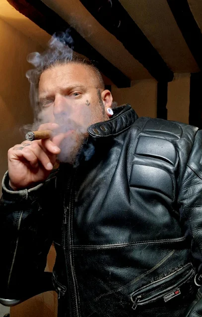 Holding cigar in mouth bearded biker wearing black leather jacket from chest up