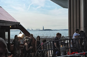 Ferry commuters dissembark at the lower Manhattan ferry terminal with a glimps of the Statue of Liberty and shipping gantries in the distance. Travel photography by Kent Johnson.
