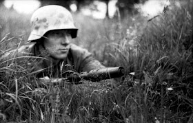 A concealed German soldier in northern France, 1944. His Karabiner 98k is equipped with a Gewehrgranatgerät cup-type grenade launcher attachment.