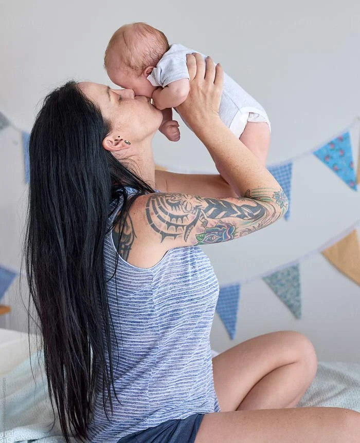 Madre tatuada besando a sus bebe