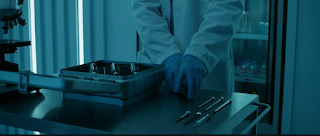 A mysterious doctor in a lab coat and gloves. The doctor is preparing several large syringes to extra blood into a container.