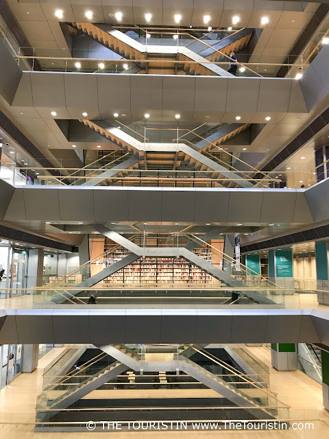 A wall of bookshelves on the second floor of a four-storey maisonette-style property connected by silver-coloured light wooden staircases.