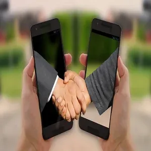 Foto imagem de dois celulares frente a frente e de cada um, se projeta uma mão que se cumprimentam.