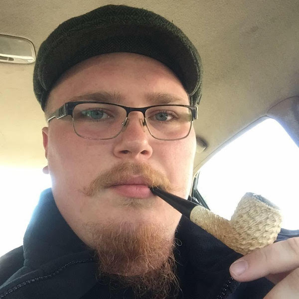 Unbearded pipe smoker driving wearing glasses from the neck up