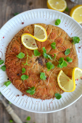 Goldgelb ausgebratenes Parasol-Schnitzerl auf einem Teller, mit Sauerklee und rosa Pfeffer bestreut und mit Zitronenscheiben garniert.